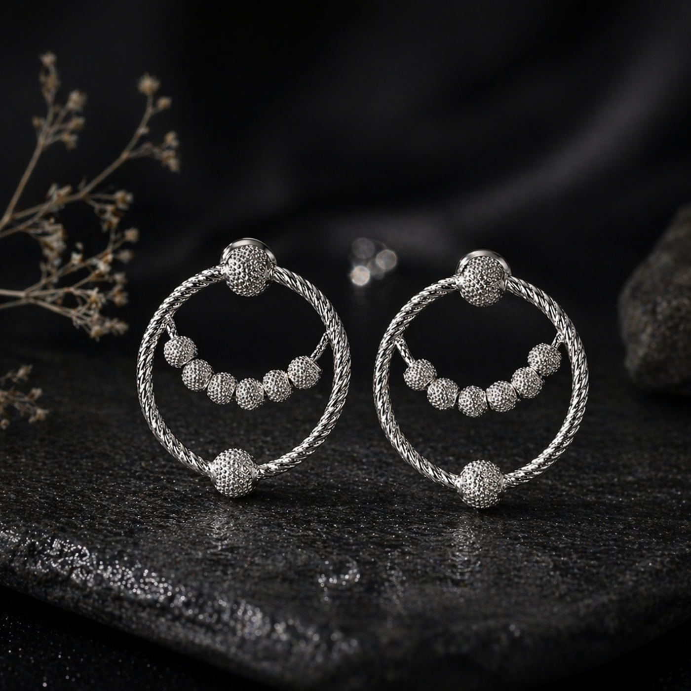 Pair of silver hoop earrings with spherical beads on a dark surface.